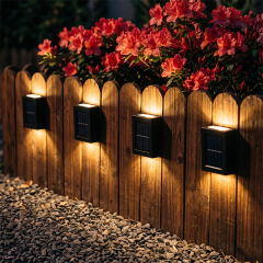 A row of solar deck lights providing warm up and down lighting along a low wooden fence with flowers.