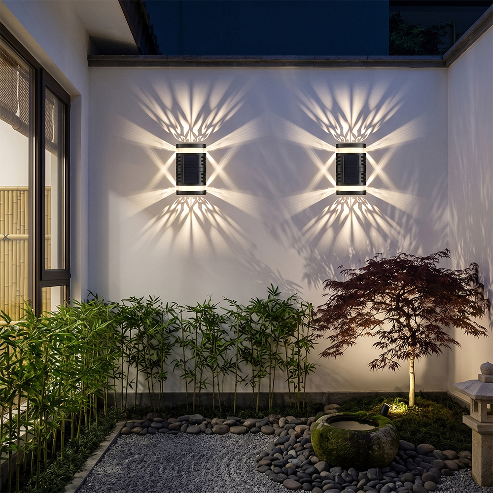 Two solar shadow pattern lights creating decorative lighting effects on a white garden wall with green plants.