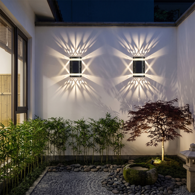 Two solar shadow pattern lights creating decorative lighting effects on a white garden wall with green plants.