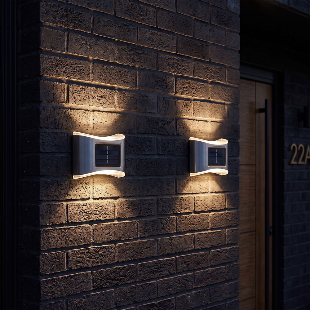Two stainless steel solar up and down wall lights casting warm optical light beams on a brick exterior wall.