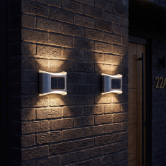 Two stainless steel solar up and down wall lights casting warm optical light beams on a brick exterior wall.