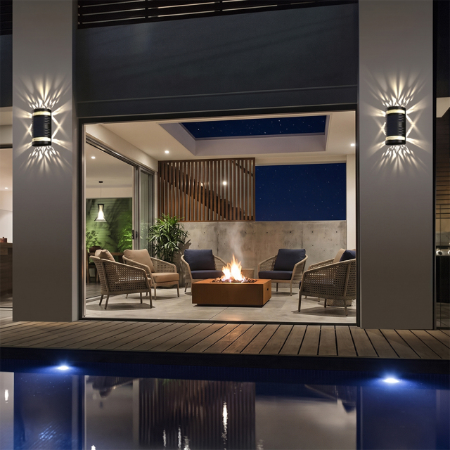 Solar up and down wall lights mounted on patio pillars illuminating a luxury swimming pool deck at night.