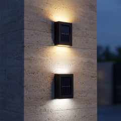 A black solar up and down wall sconce glowing with warm light on a concrete wall in evening.