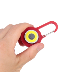 A hand holding a compact red COB LED keychain light to demonstrate its lightweight mini size.