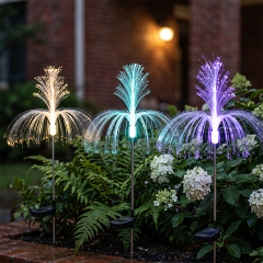 An orange and a blue solar optical fiber jellyfish light nestled among green leaves and hydrangea flowers in a garden.