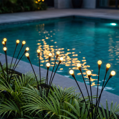 Solar firefly lights installed among green palm leaves beside a swimming pool with warm light reflections.