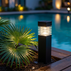 A black solar bollard light illuminating a pool deck surrounded by green palm leaves at night.