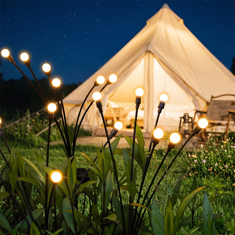 Solar firefly lights shining on a green lawn in front of an illuminated outdoor camping tent at night.