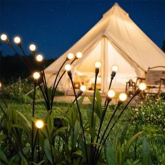 Solar firefly lights shining on a green lawn in front of an illuminated outdoor camping tent at night.