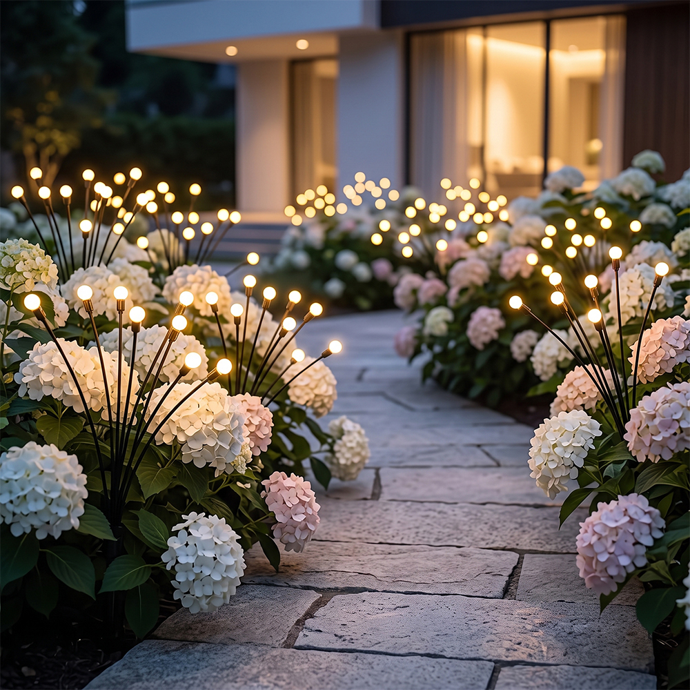 Warm solar firefly lights illuminating a stone garden pathway bordered by blooming hydrangea flowers at night.