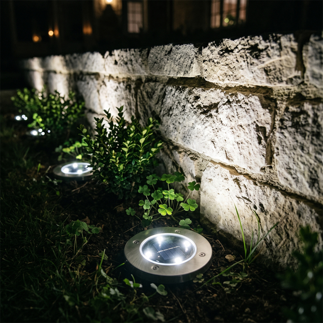 Solar ground disk lights shining bright upward light against a stone retaining wall in a garden bed.