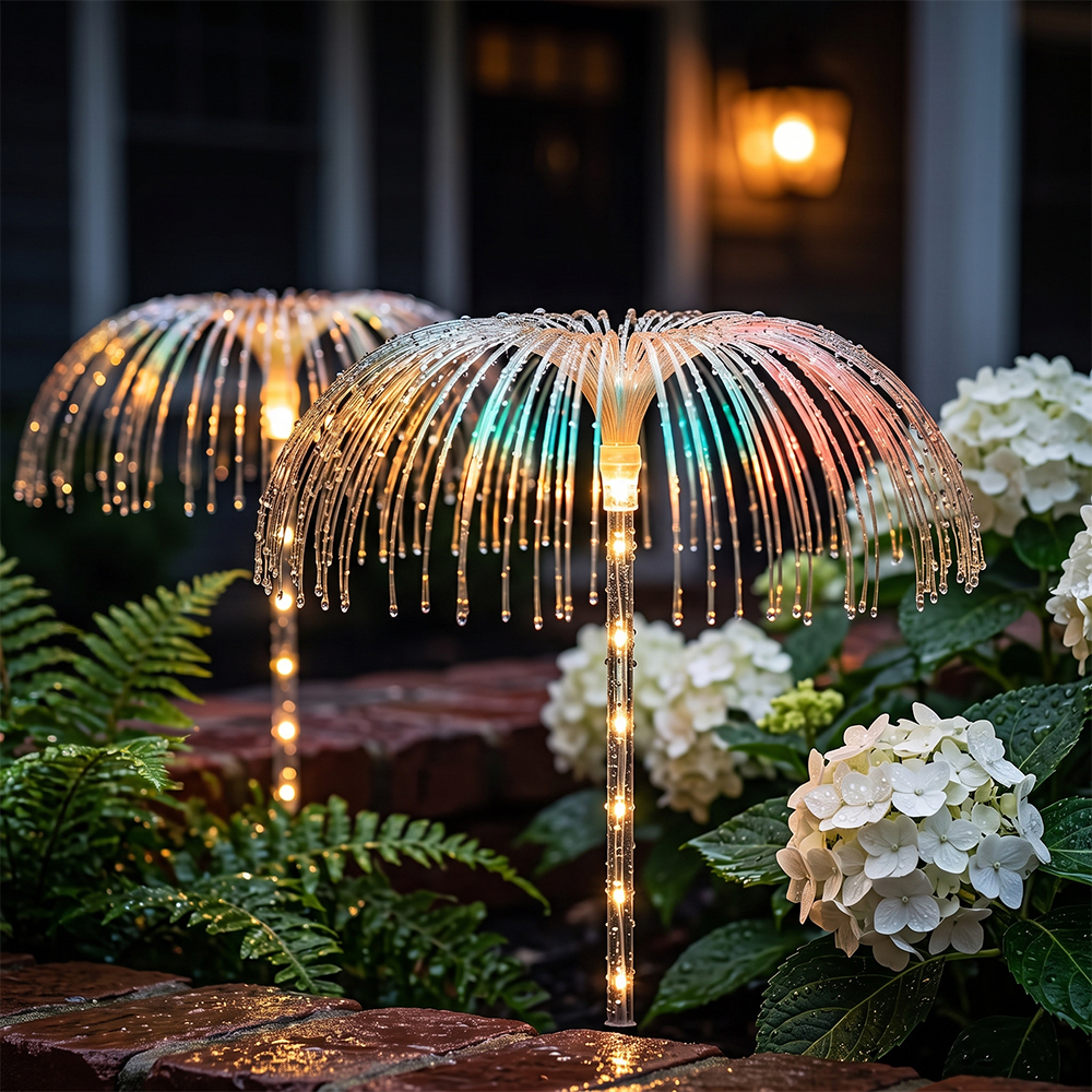 Glowing solar optical fiber fountain lights in a planter bed with ferns and hydrangeas against a red brick house wall.