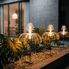 Warm solar optical fiber fountain lights installed on a gravel bed next to large monstera leaves outside a modern building.