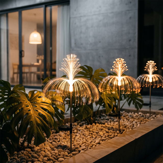 Warm solar optical fiber fountain lights installed on a gravel bed next to large monstera leaves outside a modern building.