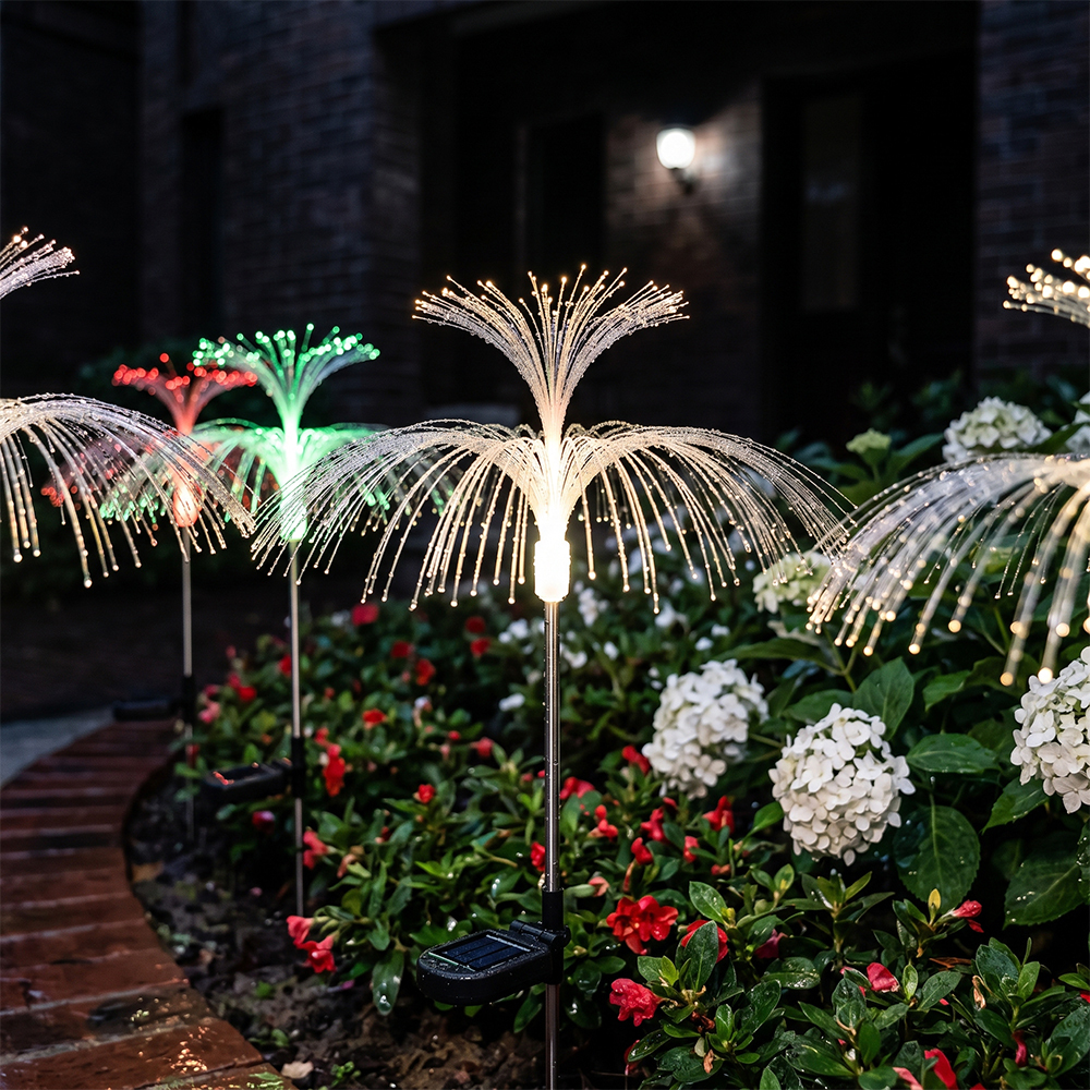 Multiple solar optical fiber jellyfish lights glowing along a garden path bordered by a brick retaining wall at night.