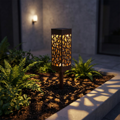 A black hollowed-out solar pathway light glowing in a modern garden flowerbed at night.