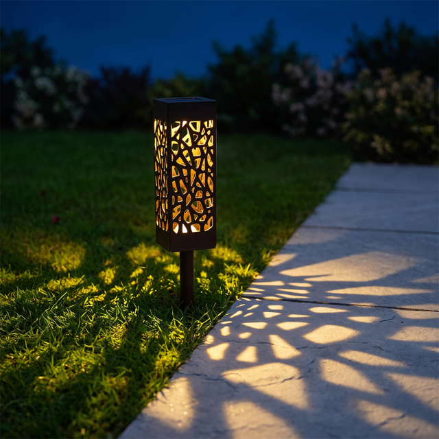 A solar pathway light installed on a grass lawn casting warm pattern light across a concrete walkway.