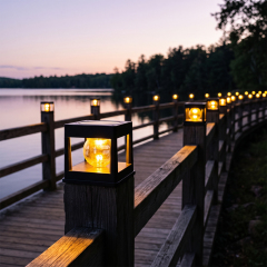 Solar post lights mounted along the wooden railing of a lakefront bridge at sunset.