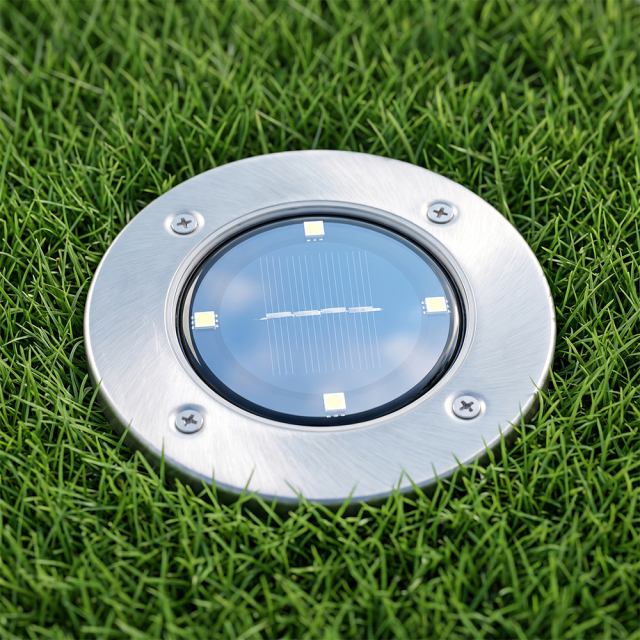 Top view of a stainless steel solar ground disk light installed flush in a green lawn.