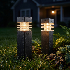 Two black waterproof solar pathway bollard lights covered in raindrops glowing on a garden lawn at night.