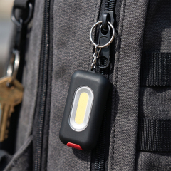 A black rectangular COB LED keychain light attached to a grey backpack zipper.