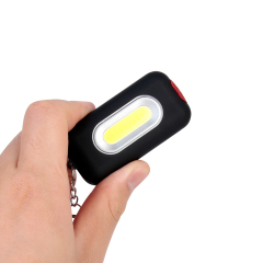 A hand holding a compact black COB LED keychain light to show its portable size.