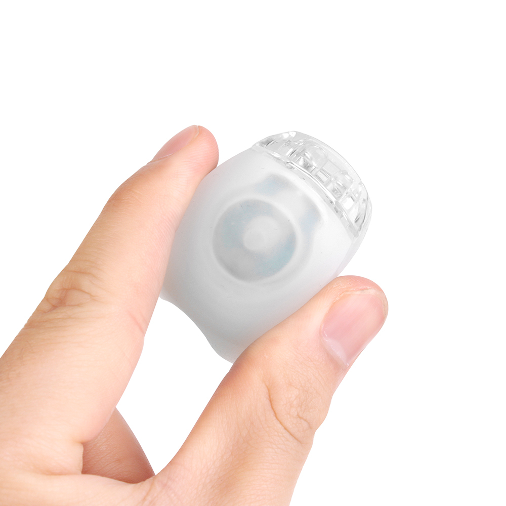 A hand pressing the power switch of a compact white silicone bike light.