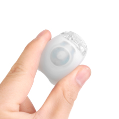 A hand pressing the power switch of a compact white silicone bike light.