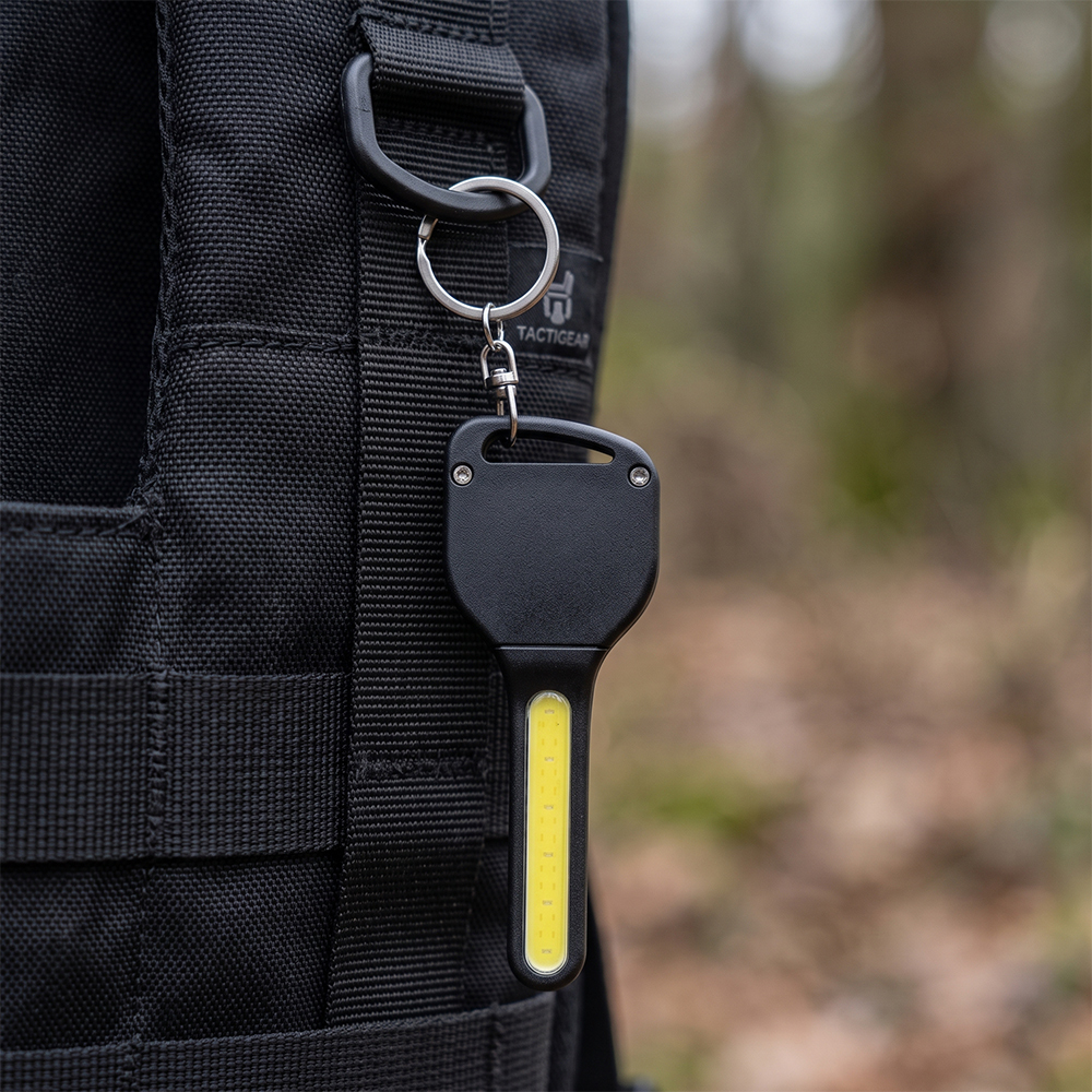 A key-shaped COB LED keychain light attached to a black outdoor backpack ring.