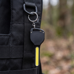 A key-shaped COB LED keychain light attached to a black outdoor backpack ring.