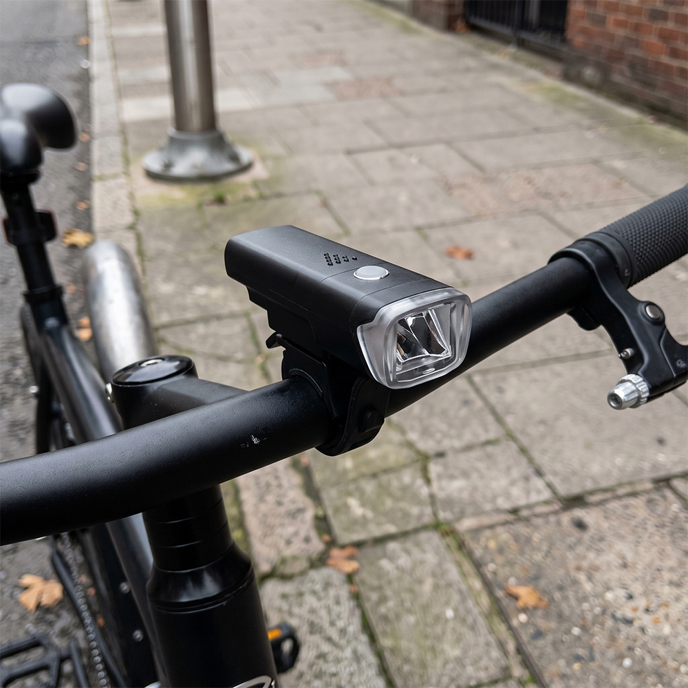 A black LED bike front light mounted on a bicycle handlebar outdoors.