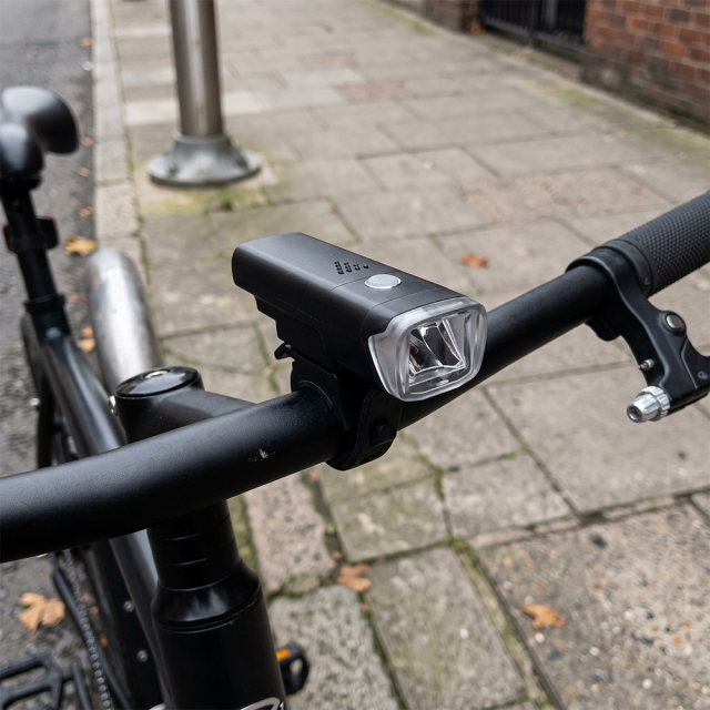 A black LED bike front light mounted on a bicycle handlebar outdoors.