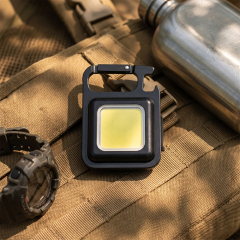 A black rechargeable COB keychain light placed on a tactical backpack next to a water bottle.