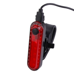 A USB charging cable plugged into the top port of a rechargeable LED bike rear light.