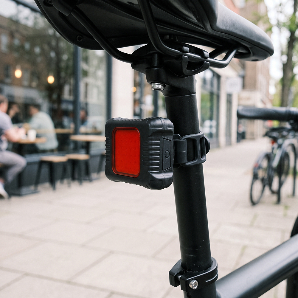 Red COB LED bicycle tail light mounted on a bike seatpost in an urban outdoor setting.
