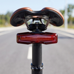 A red geometric rechargeable LED bike tail light mounted on a bicycle seatpost outdoors.