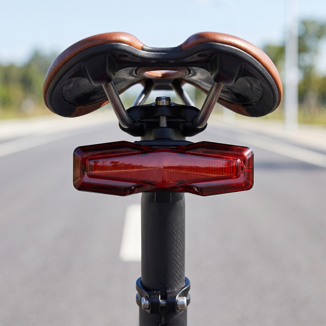 A red geometric rechargeable LED bike tail light mounted on a bicycle seatpost outdoors.