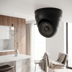 Realistic black dummy dome security camera mounted on the indoor ceiling of a modern apartment.