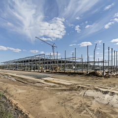 Long-span steel frame industrial building under construction with columns, roof beams, and crane installation