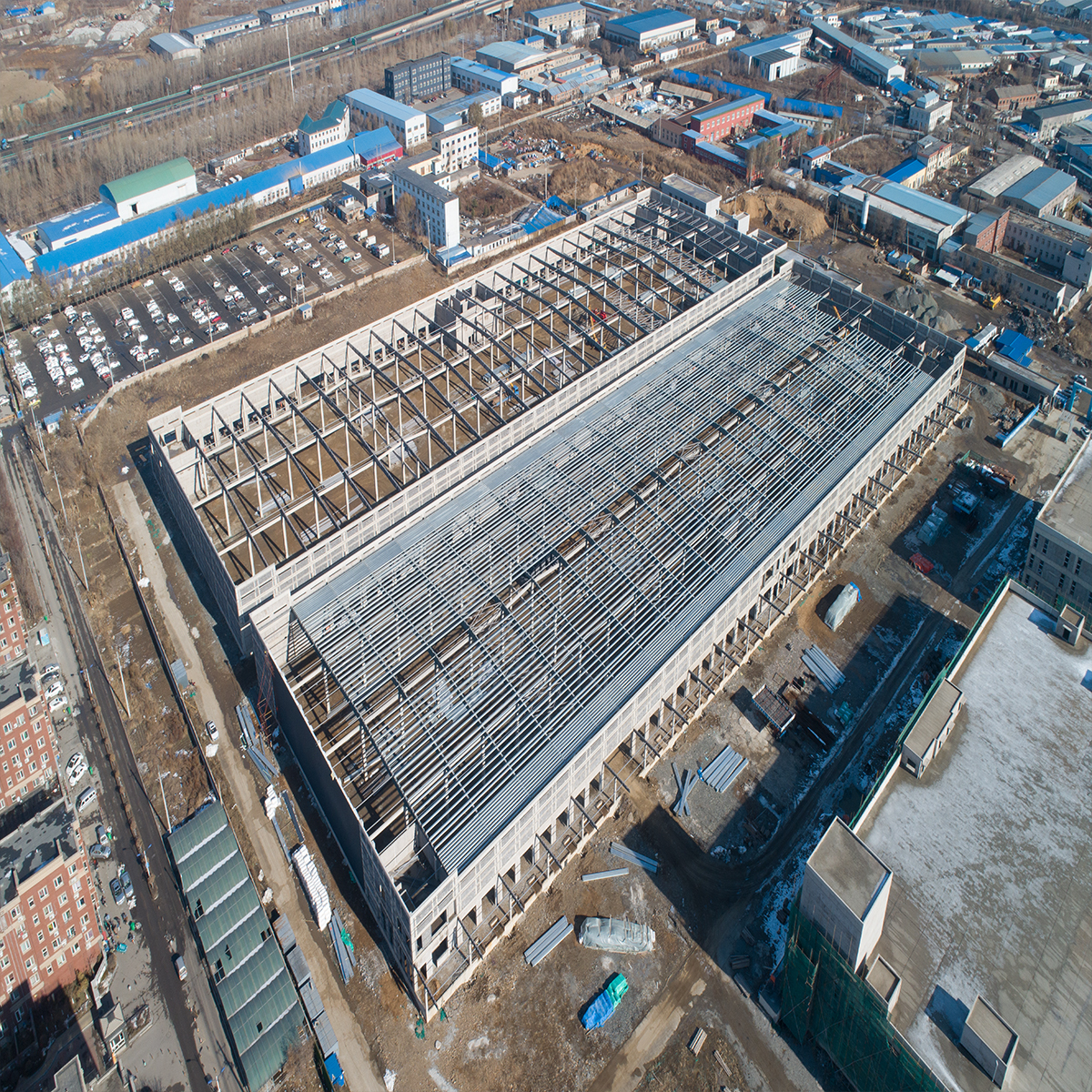 Aerial view of a large steel structure factory building under construction with roof trusses and partial metal roofing