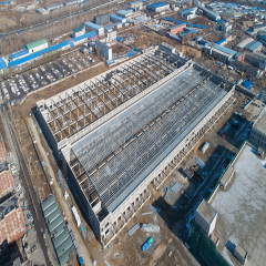 Aerial view of a large steel structure factory building under construction with roof trusses and partial metal roofing