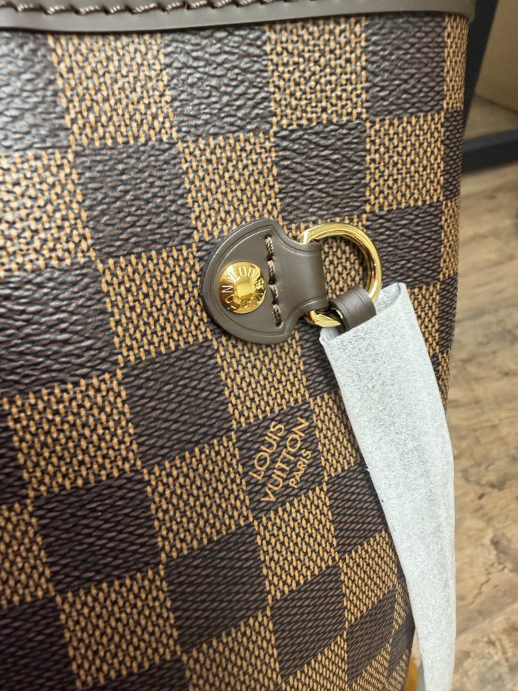The Louis Vuitton Neverfull MM medium tote bag features the classic Damier Ebene brown checkered canvas, paired with the iconic red striped lining.