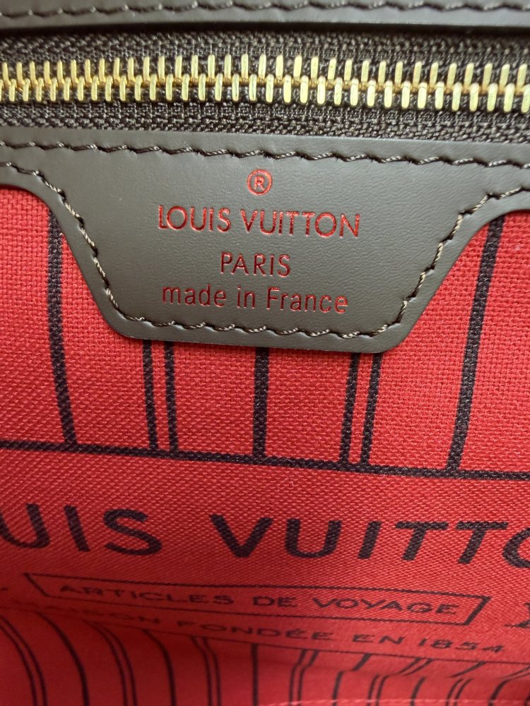 The Louis Vuitton Neverfull MM medium tote bag features the classic Damier Ebene brown checkered canvas, paired with the iconic red striped lining.