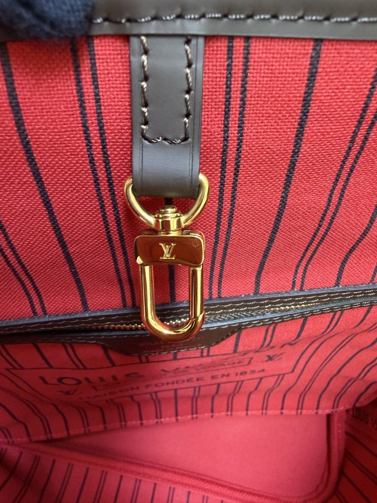 The Louis Vuitton Neverfull MM medium tote bag features the classic Damier Ebene brown checkered canvas, paired with the iconic red striped lining.