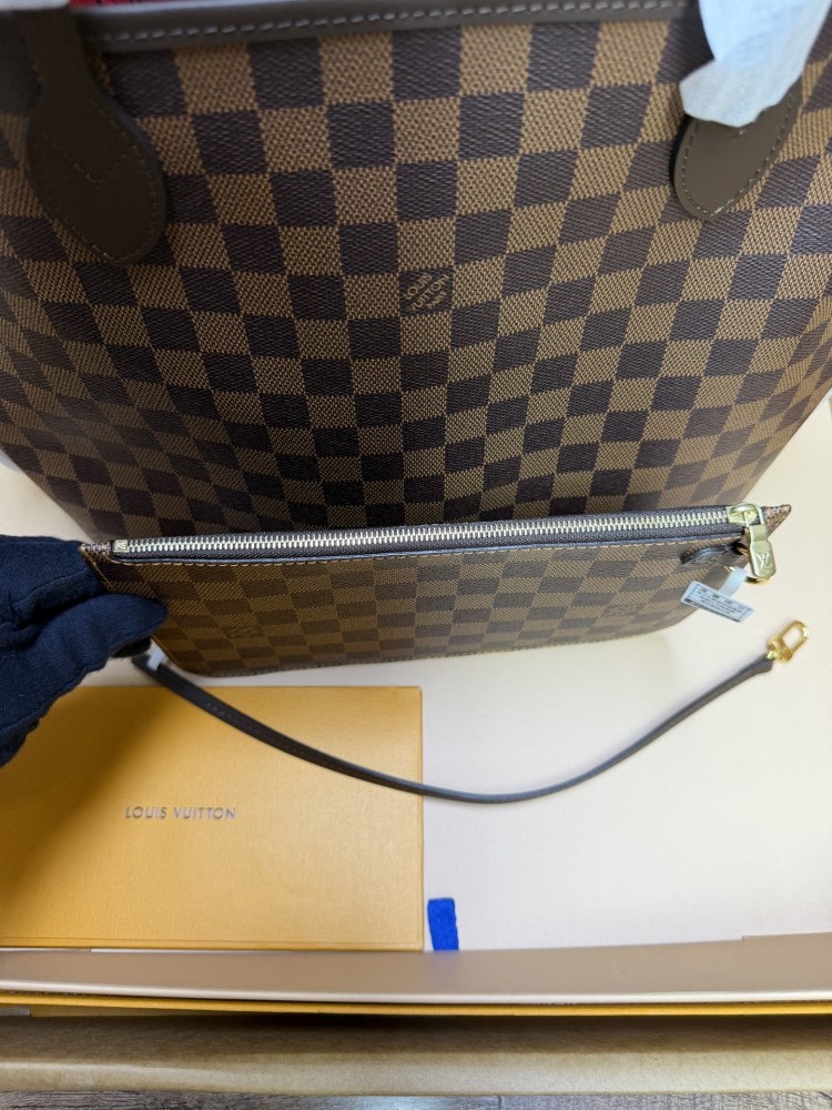 The Louis Vuitton Neverfull MM medium tote bag features the classic Damier Ebene brown checkered canvas, paired with the iconic red striped lining.
