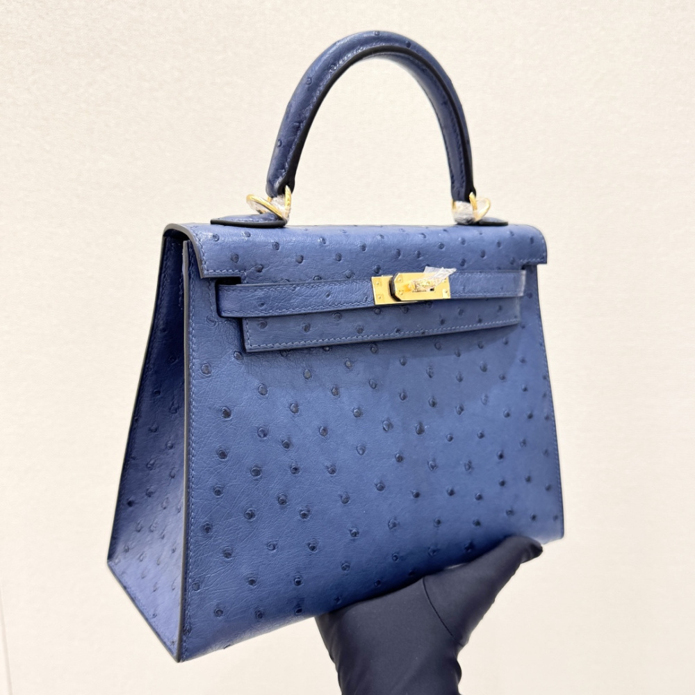 The Hermès Kelly 25 handbag in ostrich leather—rendered in a deep marine blue (gemstone blue / midnight blue) and accented with gold hardware—stands as a quintessential example of understated luxury among Hermès' exotic skins.