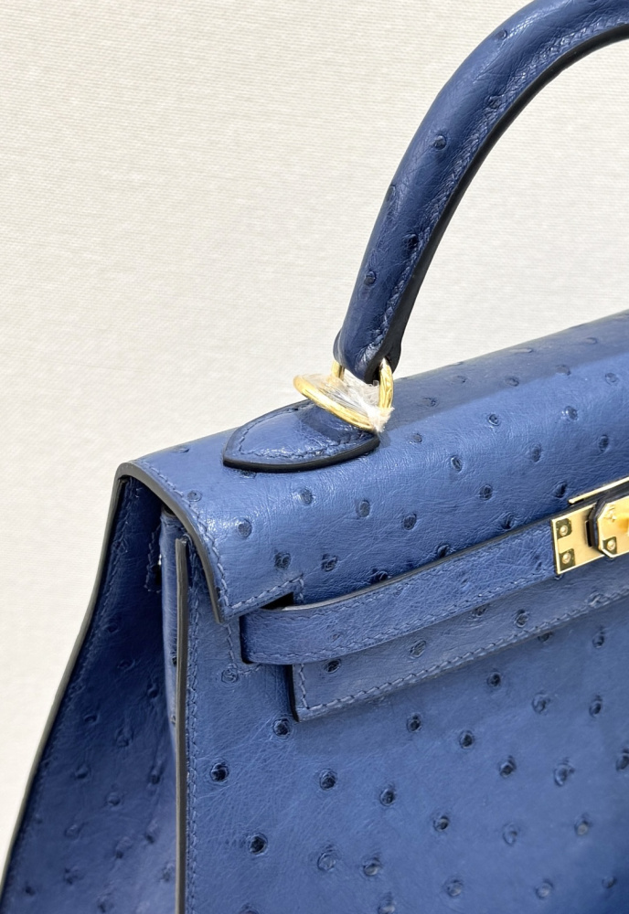 The Hermès Kelly 25 handbag in ostrich leather—rendered in a deep marine blue (gemstone blue / midnight blue) and accented with gold hardware—stands as a quintessential example of understated luxury among Hermès' exotic skins.