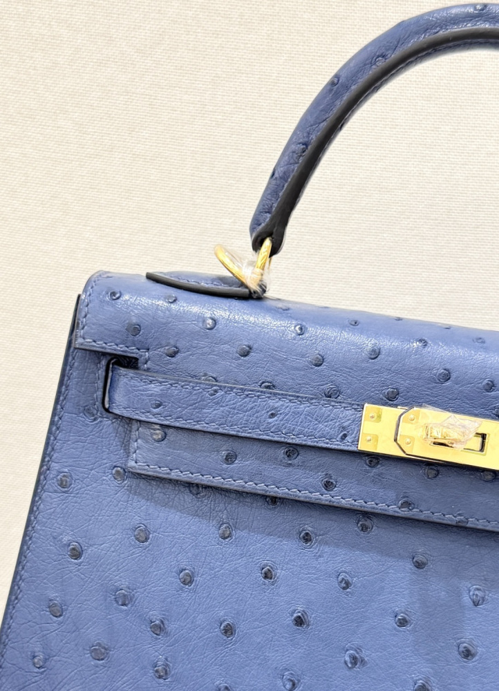 The Hermès Kelly 25 handbag in ostrich leather—rendered in a deep marine blue (gemstone blue / midnight blue) and accented with gold hardware—stands as a quintessential example of understated luxury among Hermès' exotic skins.