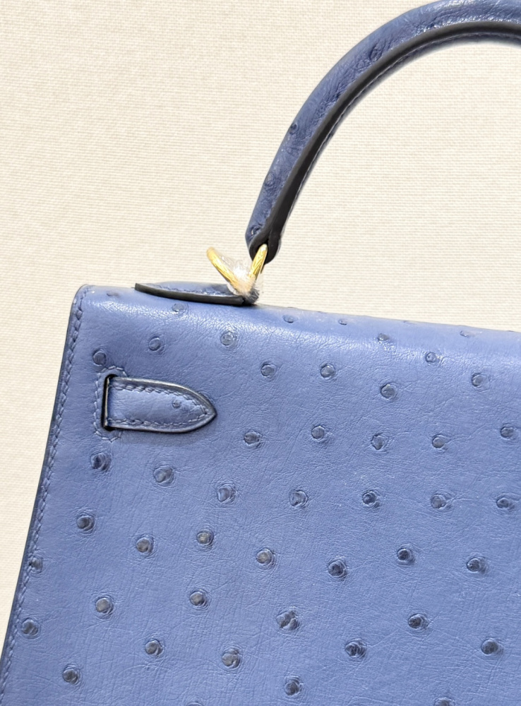 The Hermès Kelly 25 handbag in ostrich leather—rendered in a deep marine blue (gemstone blue / midnight blue) and accented with gold hardware—stands as a quintessential example of understated luxury among Hermès' exotic skins.
