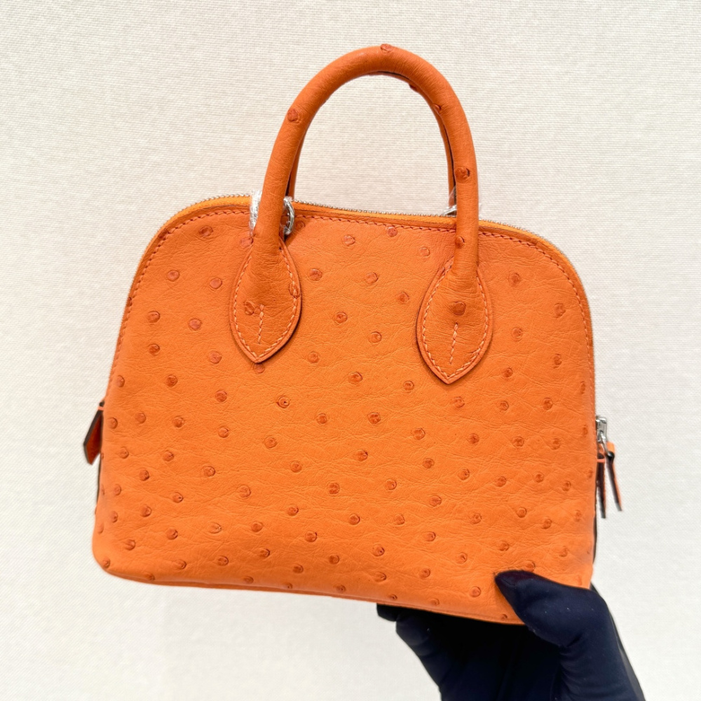 The Hermès Mini Bolide handbag in ostrich leather—featuring the classic Hermès Orange paired with silver hardware—is a highly recognizable and vibrant piece within the brand's exotic skins collection.